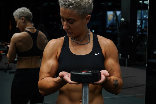 lifter holding a dumbbell in both hands and looking down at it in a dark gym
