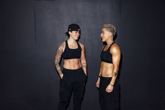 two lifters with visibly different frames standing side by side against a dark studio wall