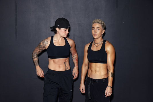 two muscular lifters in black training gear standing together against a dark studio wall