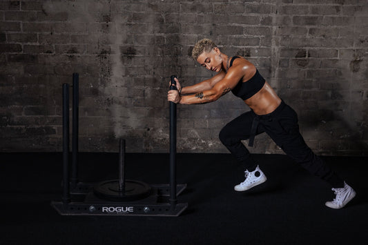 lifter driving a loaded sled across a dark gym floor