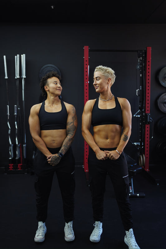 two lifters standing in front of a squat rack, visibly built, mid-laugh
