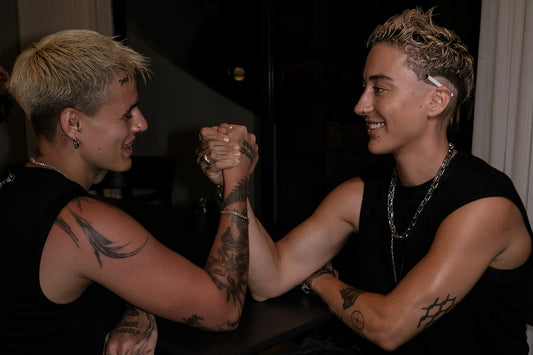 two lifters in black tanks arm-wrestling across a small cafe table at night, both smiling