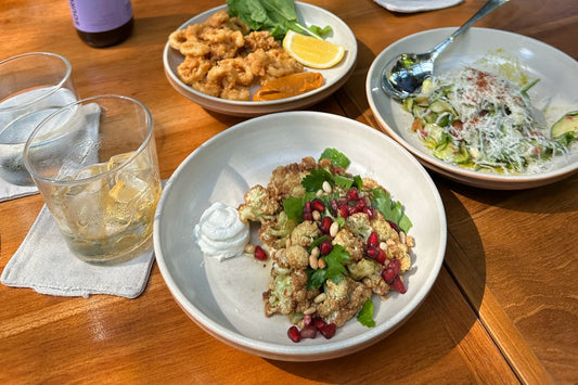 a cafe table from above: roasted cauliflower with pomegranate and yoghurt, fried calamari with lemon, a shaved courgette salad, two glasses of iced tea