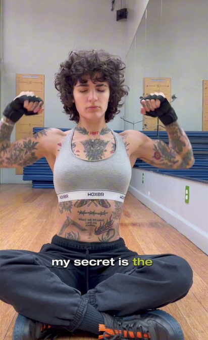 Person with tattoos sitting on the floor in a room with mirrors.